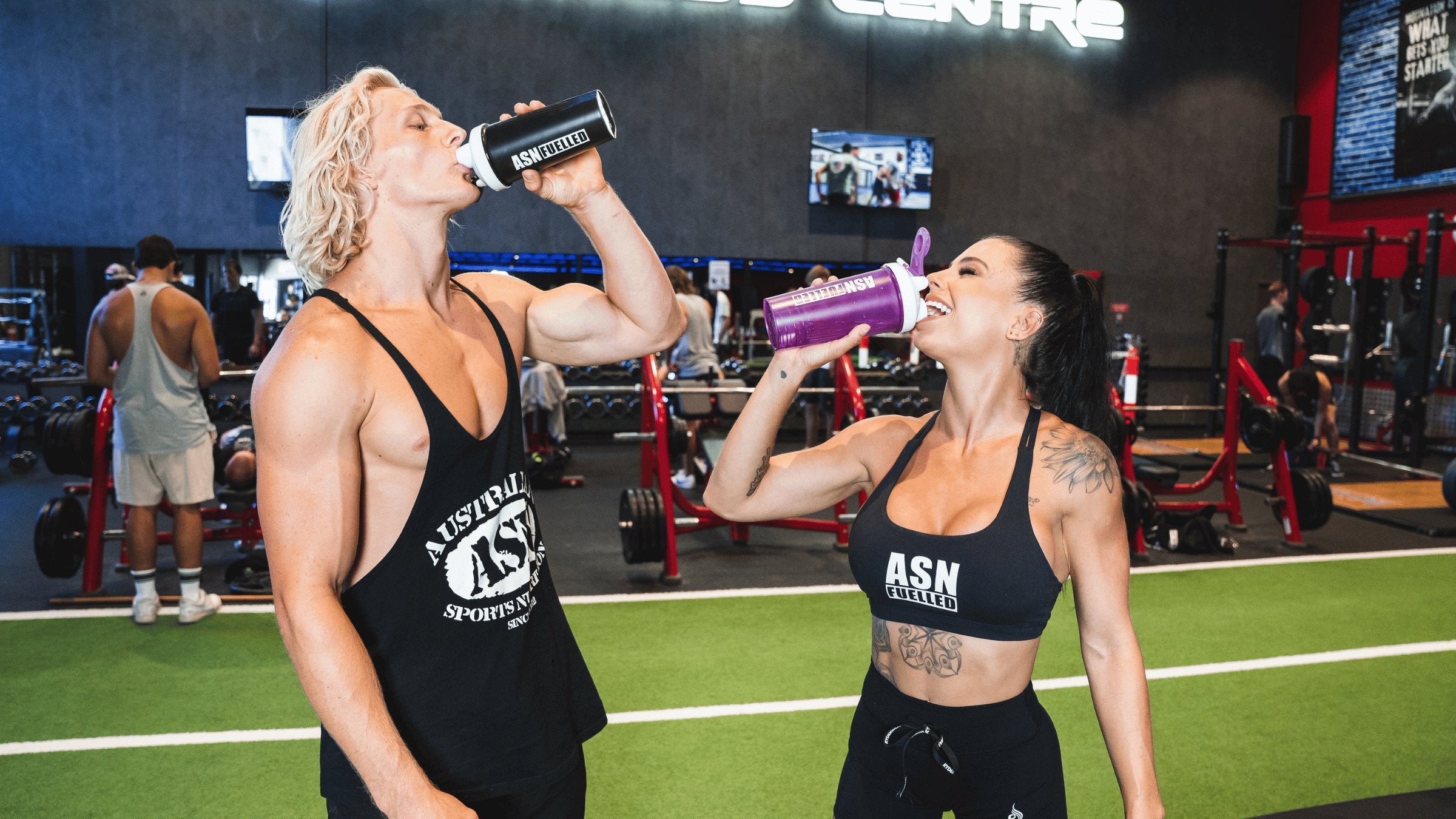 guy and girl drinking protein shakes in gym